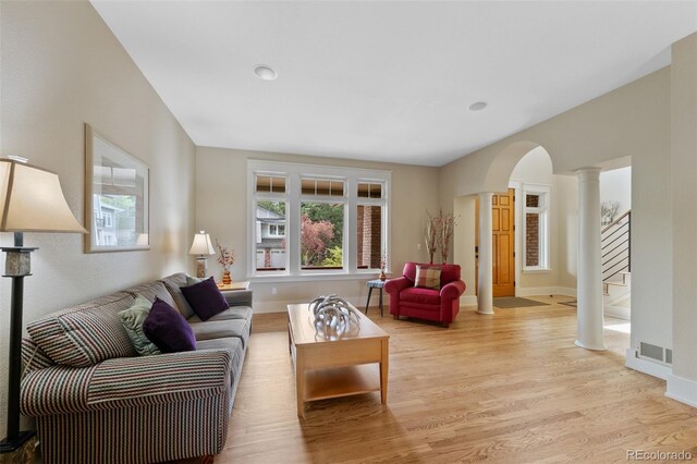 living room featuring visible vents, stairway, ornate columns, arched walkways, and light wood-style flooring