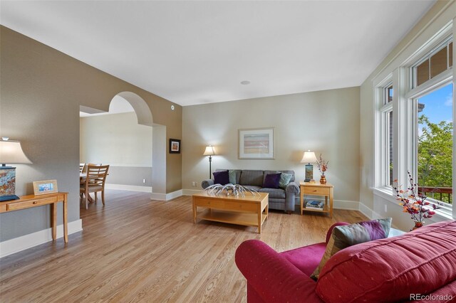living area with baseboards, light wood-type flooring, and arched walkways