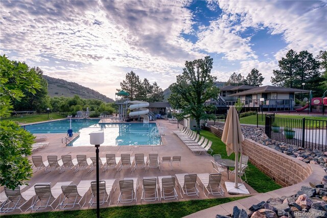 community pool with fence, a water slide, a mountain view, and a patio