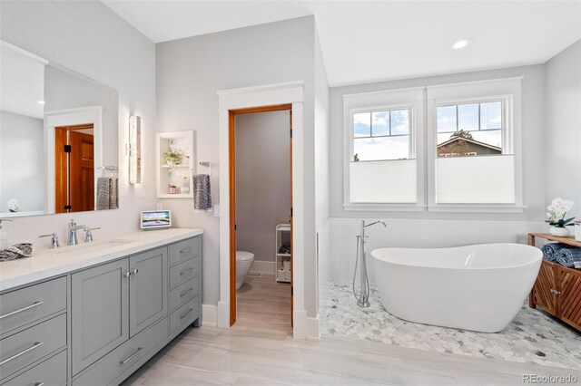 full bathroom with vanity, toilet, recessed lighting, a freestanding tub, and baseboards