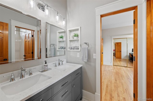 full bath featuring double vanity, a sink, baseboards, and wood finished floors