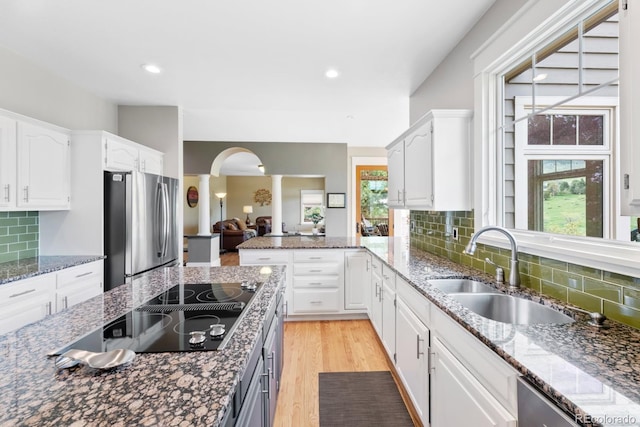 kitchen with a sink, arched walkways, white cabinets, and freestanding refrigerator