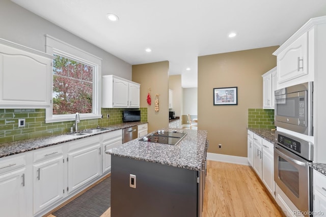 kitchen with decorative backsplash, a kitchen island, appliances with stainless steel finishes, white cabinets, and stone countertops