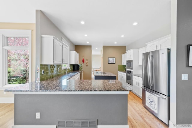 kitchen featuring visible vents, appliances with stainless steel finishes, dark stone countertops, a peninsula, and light wood-style flooring