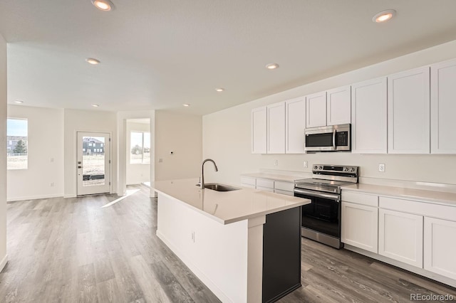 kitchen with a center island with sink, white cabinets, sink, light wood-type flooring, and stainless steel appliances