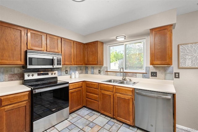 kitchen featuring stainless steel appliances, a sink, light countertops, decorative backsplash, and brown cabinetry