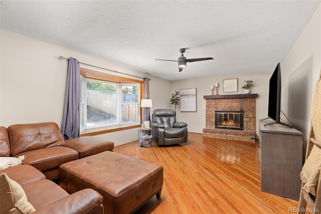 living room with light wood finished floors, a ceiling fan, and a fireplace