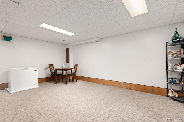carpeted dining area featuring a drop ceiling and baseboards