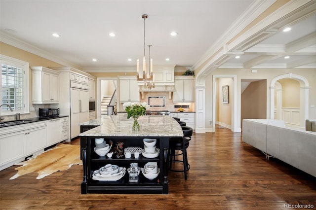 kitchen featuring a large island, dark hardwood / wood-style floors, light stone countertops, hanging light fixtures, and sink