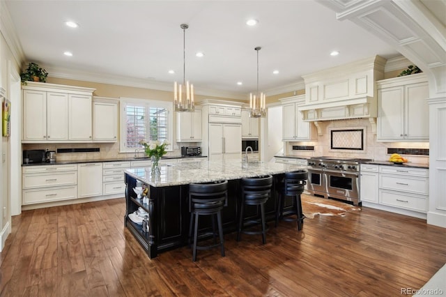 kitchen featuring high end appliances, hanging light fixtures, ornamental molding, dark hardwood / wood-style floors, and a large island with sink