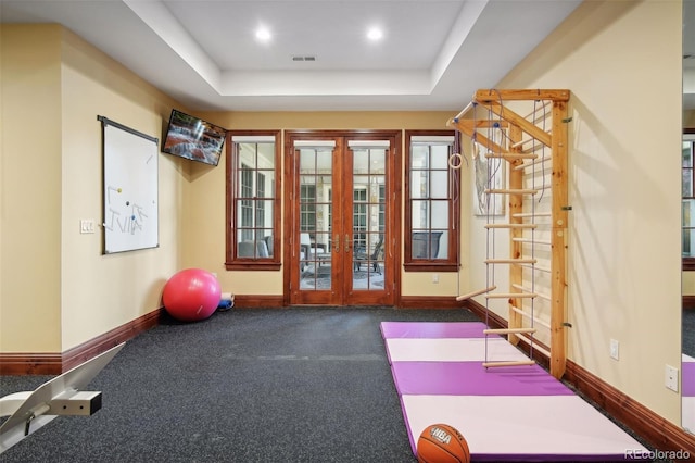 workout room with a tray ceiling, french doors, and carpet flooring