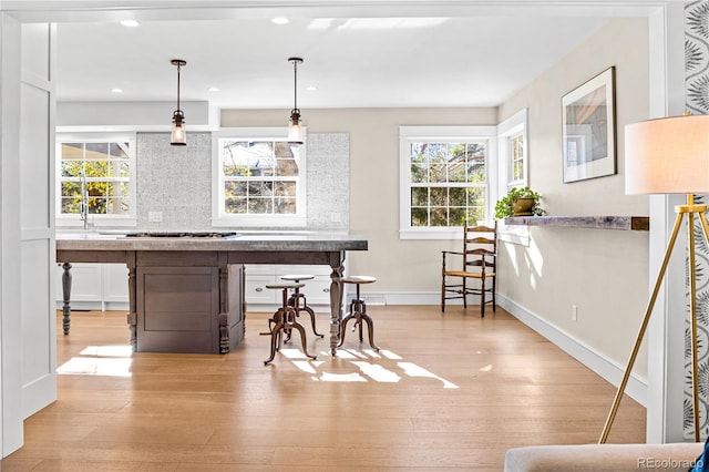 bar featuring tasteful backsplash, gas cooktop, decorative light fixtures, and light hardwood / wood-style flooring