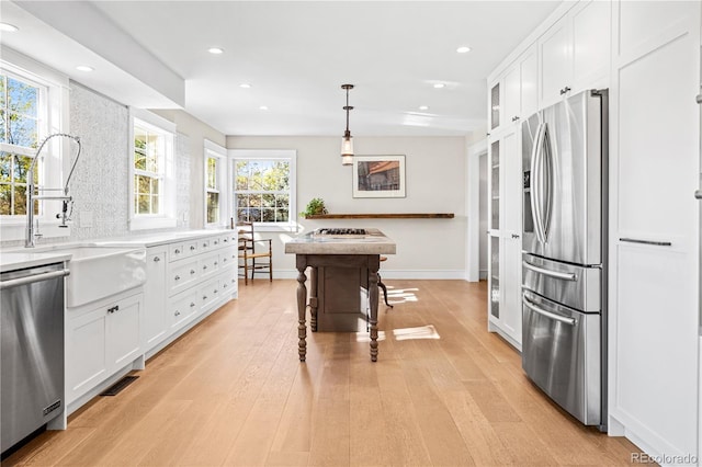 kitchen featuring white cabinetry, stainless steel appliances, hanging light fixtures, and a wealth of natural light