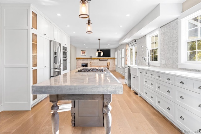 kitchen with decorative light fixtures, white cabinetry, stainless steel appliances, light wood-type flooring, and a spacious island