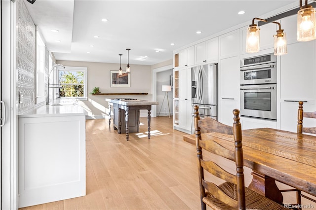 kitchen featuring pendant lighting, sink, appliances with stainless steel finishes, white cabinets, and light wood-type flooring