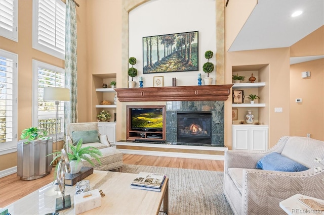 living area featuring a tiled fireplace, hardwood / wood-style floors, a towering ceiling, and built in features