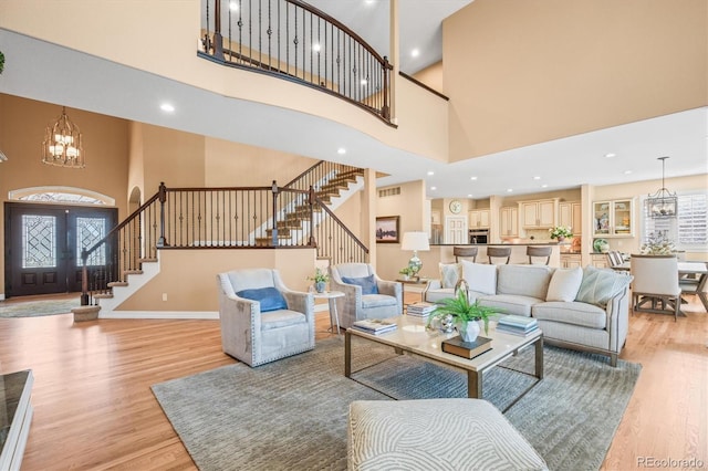 living room featuring french doors, light wood-type flooring, a high ceiling, and a notable chandelier