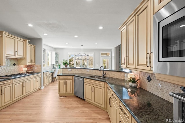 kitchen featuring sink, appliances with stainless steel finishes, pendant lighting, dark stone counters, and light hardwood / wood-style floors