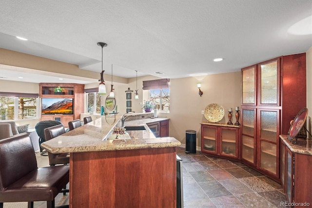 kitchen featuring pendant lighting, light stone counters, plenty of natural light, and a kitchen breakfast bar