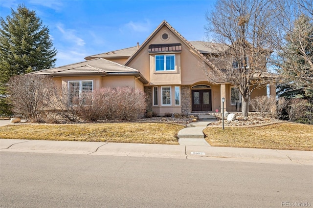 view of front of property featuring stone siding, a tiled roof, french doors, and stucco siding