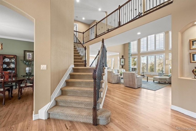 staircase with ornamental molding, baseboards, a high ceiling, and wood finished floors