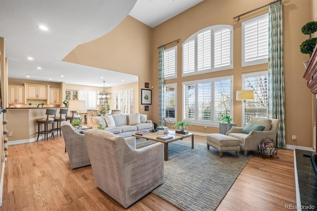 living area featuring a towering ceiling, light wood-style floors, baseboards, and recessed lighting