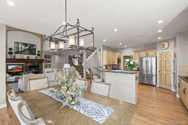 dining space featuring light wood-type flooring, a glass covered fireplace, recessed lighting, and stairs