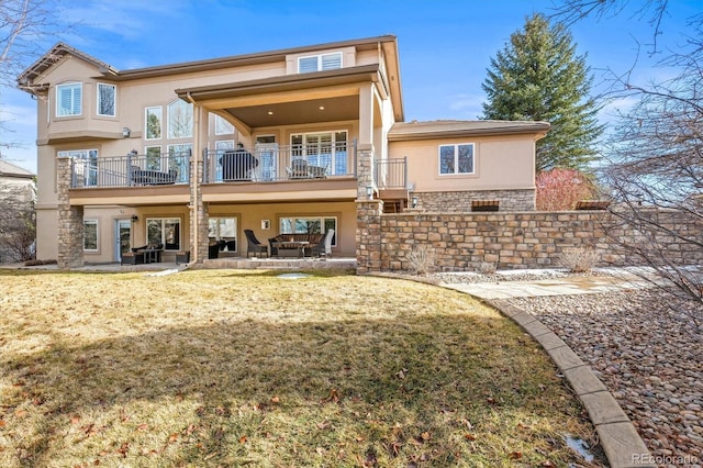 back of house featuring stone siding, a patio area, a lawn, and stucco siding