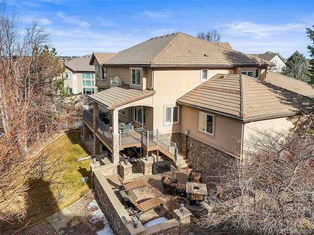 back of property with a patio, stone siding, a tile roof, outdoor lounge area, and stucco siding