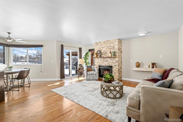 living room with light wood-type flooring, ceiling fan, and a fireplace