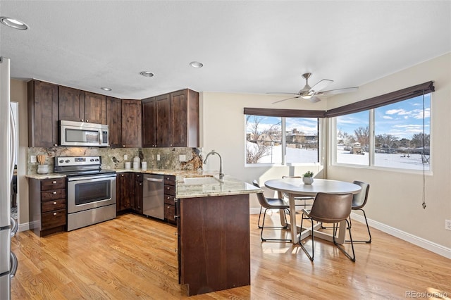 kitchen featuring kitchen peninsula, stainless steel appliances, light stone counters, dark brown cabinetry, and sink