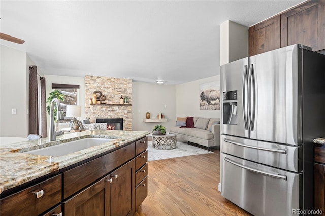 kitchen featuring sink, light wood-type flooring, stainless steel fridge with ice dispenser, a stone fireplace, and light stone counters