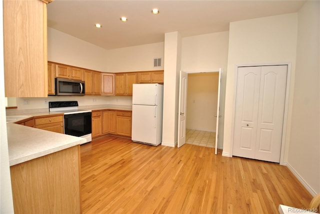 kitchen with a high ceiling, range with electric cooktop, light countertops, freestanding refrigerator, and stainless steel microwave