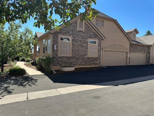 view of front of house with aphalt driveway, stone siding, an attached garage, and stucco siding