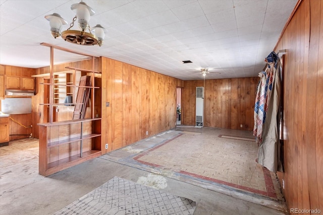 empty room featuring ceiling fan with notable chandelier and wood walls