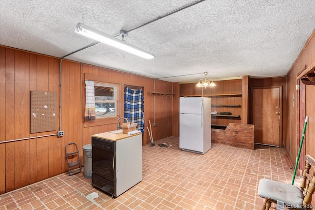 kitchen with wooden walls, white fridge, pendant lighting, and a textured ceiling