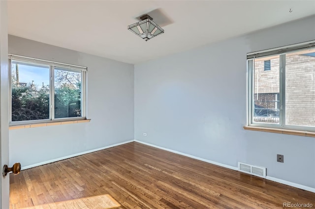 empty room featuring wood finished floors, visible vents, and baseboards