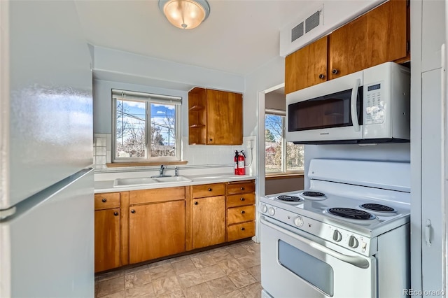 kitchen featuring white appliances, a sink, visible vents, light countertops, and brown cabinetry