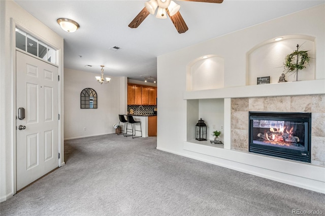 unfurnished living room featuring light colored carpet, a fireplace, and ceiling fan with notable chandelier