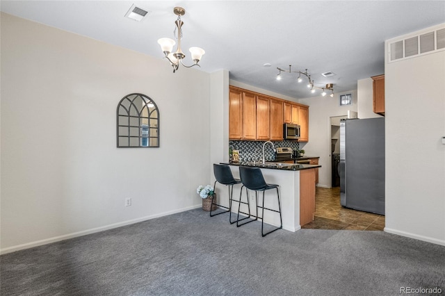 kitchen with appliances with stainless steel finishes, a kitchen breakfast bar, carpet flooring, decorative backsplash, and kitchen peninsula