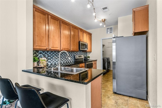 kitchen featuring appliances with stainless steel finishes, washer and dryer, a breakfast bar area, dark stone countertops, and kitchen peninsula