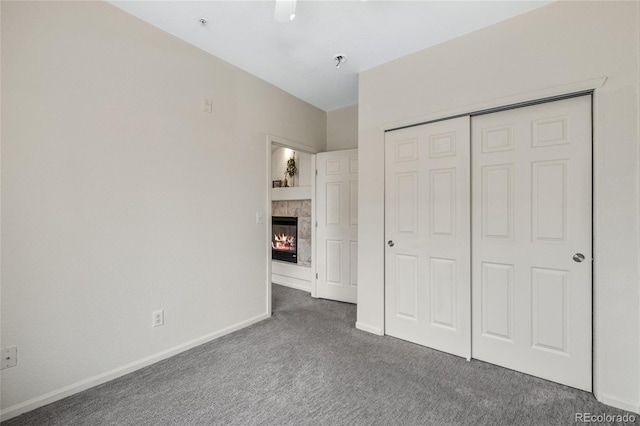 unfurnished bedroom with a fireplace, a closet, and dark colored carpet