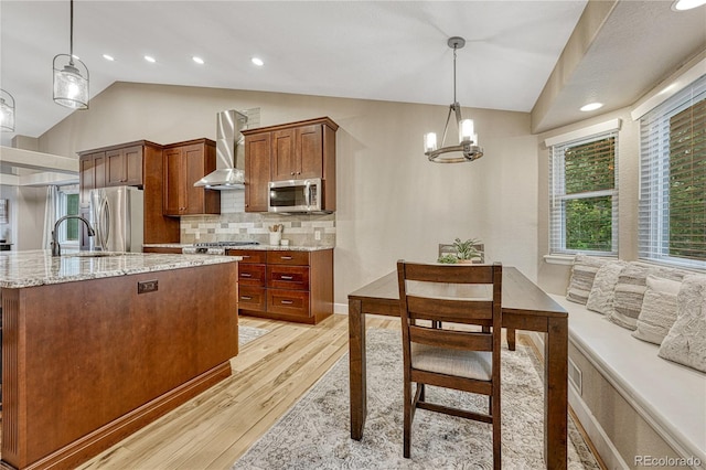 5402 S Queen Way, Littleton, CO 80127 - kitchen featuring stainless steel appliances, wall chimney range hood, light wood-style flooring, lofted ceiling, and tasteful backsplash