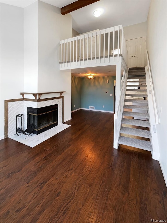 unfurnished living room featuring wood-type flooring, beam ceiling, high vaulted ceiling, and a tile fireplace