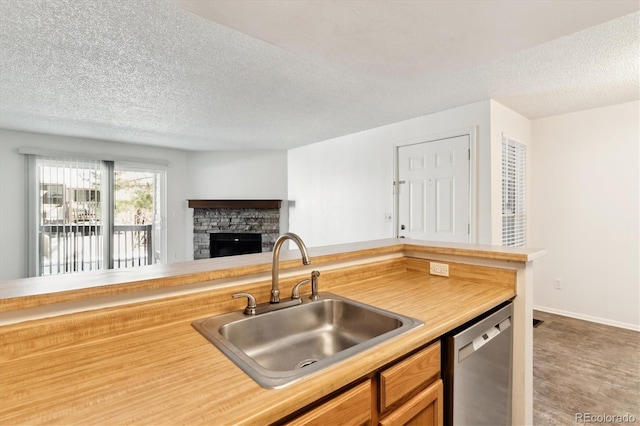 kitchen featuring a fireplace, sink, stainless steel dishwasher, kitchen peninsula, and a textured ceiling