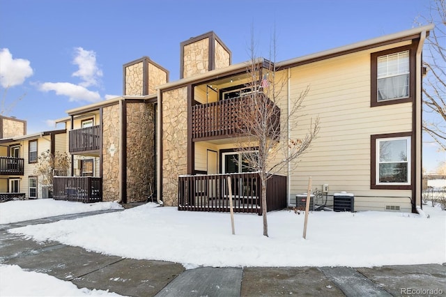 snow covered rear of property featuring central AC and a balcony