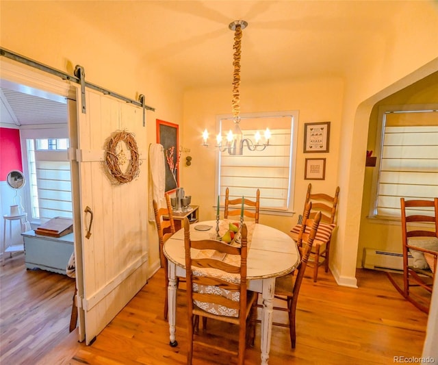 dining area featuring a barn door, light hardwood / wood-style floors, an inviting chandelier, and baseboard heating