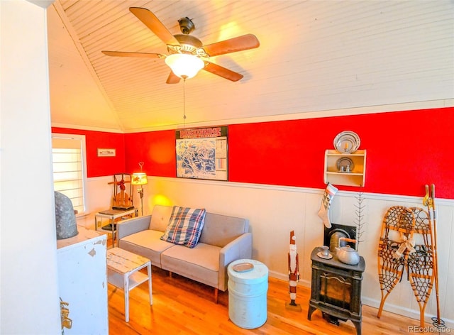 sitting room with wood-type flooring, a wood stove, ceiling fan, and lofted ceiling