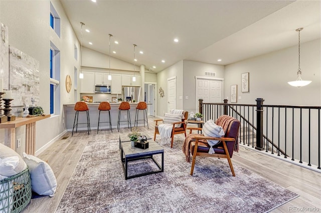 living area with recessed lighting, visible vents, a towering ceiling, light wood-style floors, and baseboards