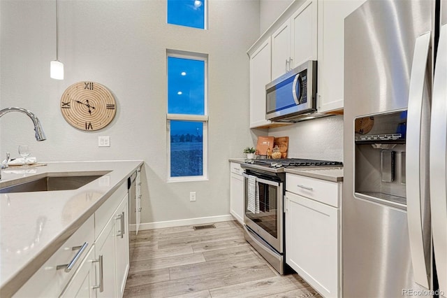 kitchen featuring white cabinets, light wood finished floors, stainless steel appliances, and a sink